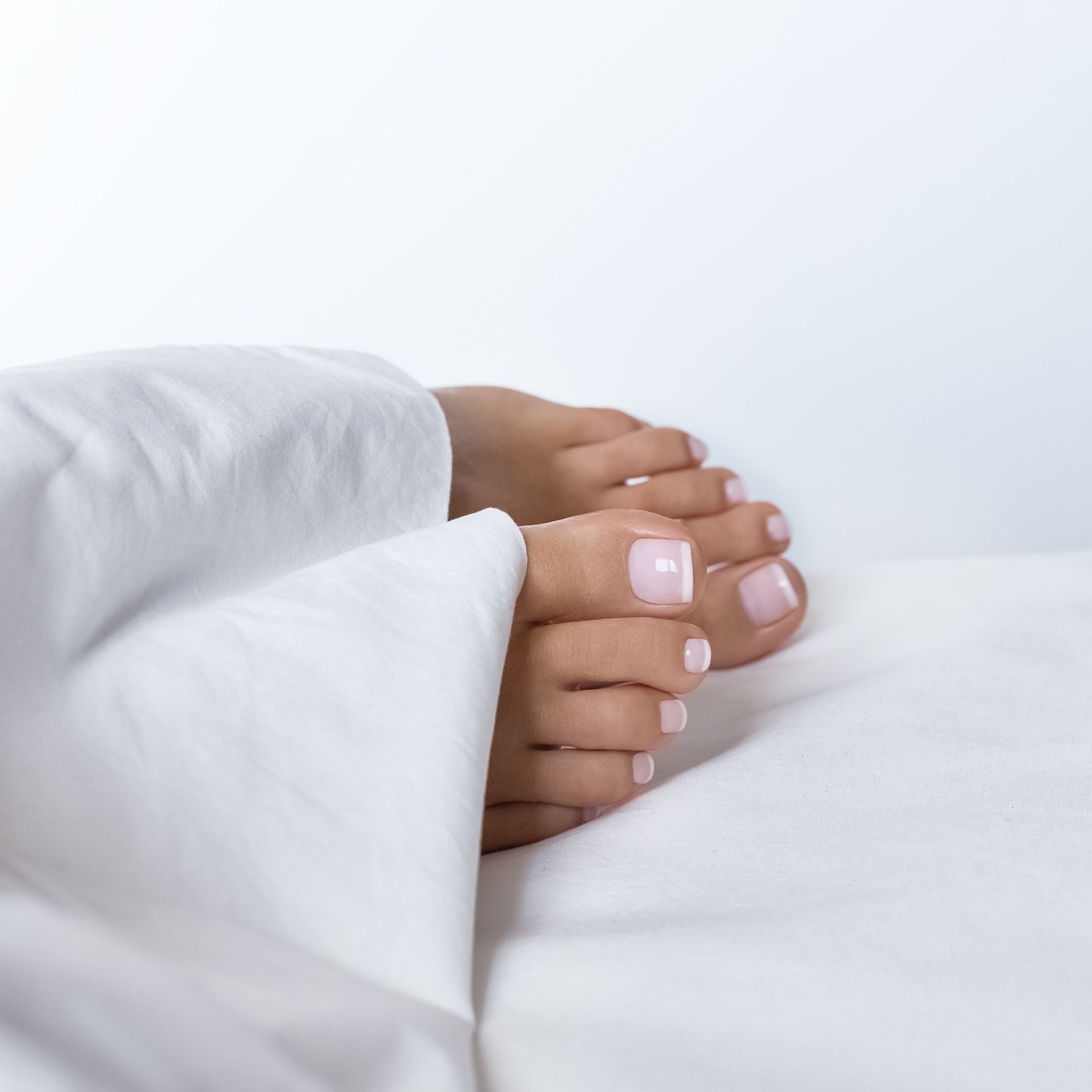 Female feet with french pedicure under white blanket. Care concept