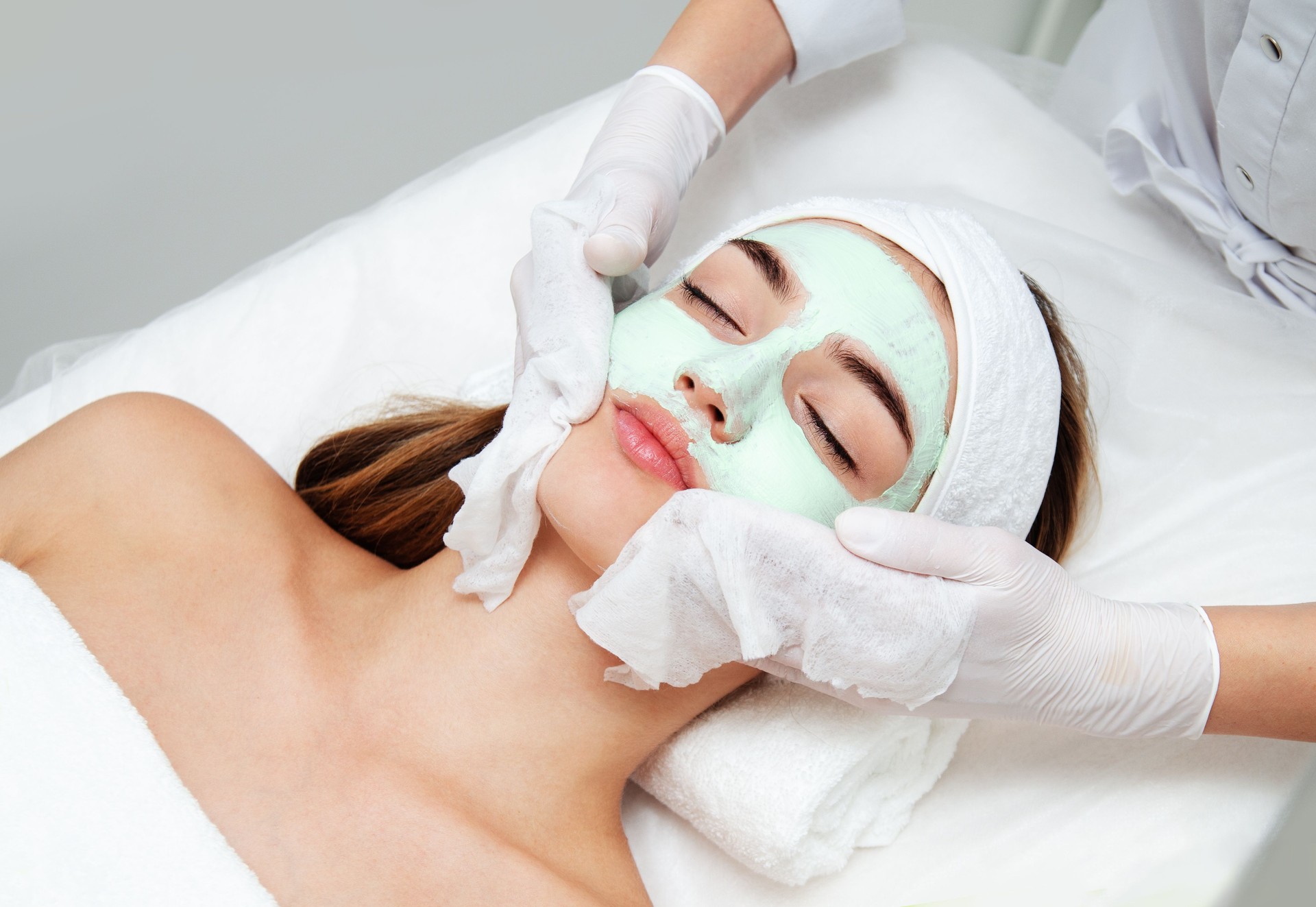 Young woman getting facial beauty treatment. Beautician cleaning and touching female face after facial mask.
